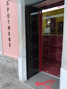 Geöffnete Eingangstür der Apotheke neben dem senkrechten Schriftzug „Apotheke“