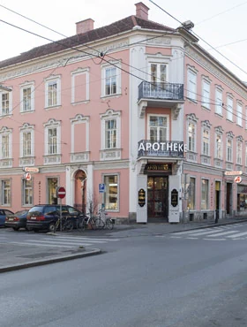 Rosafarbene Fassade mit Schriftzug „Apotheke“ über dem Eingang