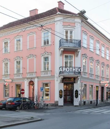 Rosafarbenes Eckhaus Leonhardstraße 6 in Graz mit dem Schriftzug „Apotheke“ über dem Eingang