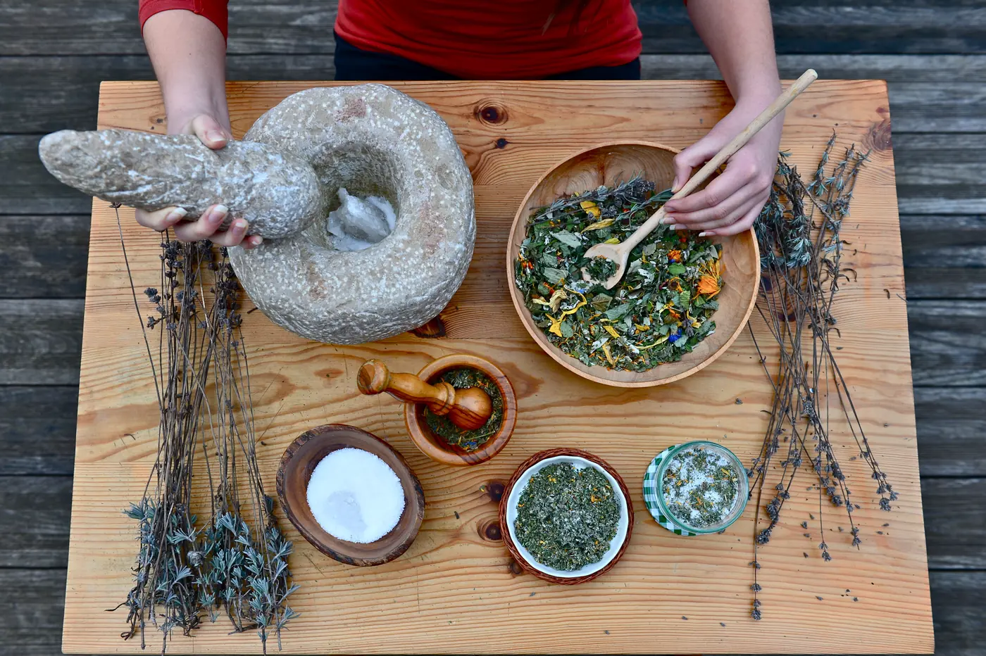 Getrocknete Kräuter, Lavendel, ein Steinmörser und Schalen mit Kräutermischungen auf einem Holzbrett